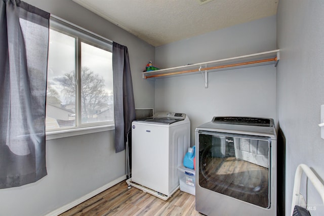 washroom with a textured ceiling, washing machine and dryer, light wood finished floors, baseboards, and laundry area