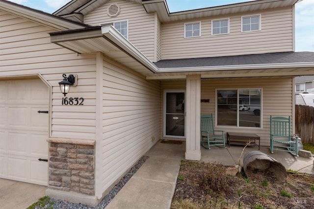 entrance to property with a garage, covered porch, and fence