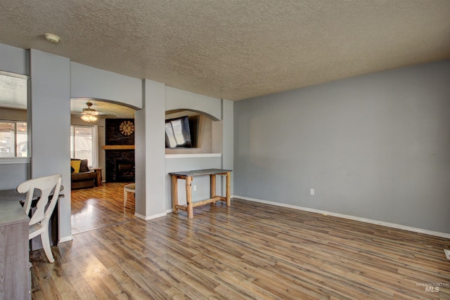 living room featuring baseboards, ceiling fan, a fireplace, wood finished floors, and a textured ceiling