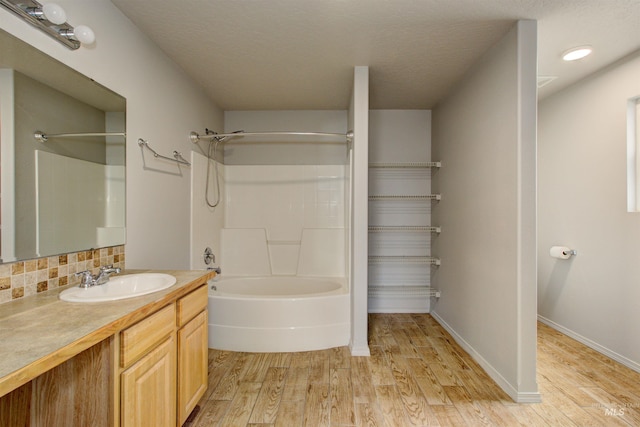 bathroom featuring wood-type flooring, vanity, washtub / shower combination, and decorative backsplash