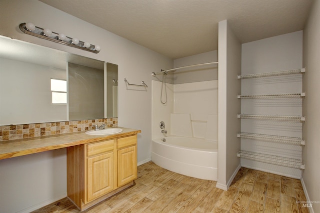 bathroom featuring wood-type flooring, bathtub / shower combination, backsplash, and vanity