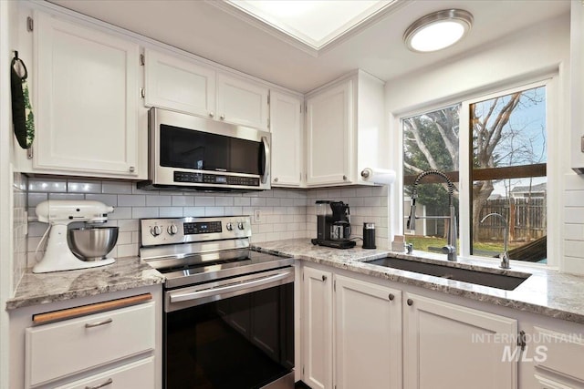 kitchen with a sink, tasteful backsplash, stainless steel appliances, white cabinets, and light stone countertops