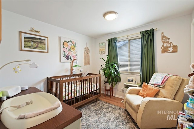 bedroom featuring a crib, wood finished floors, and baseboards