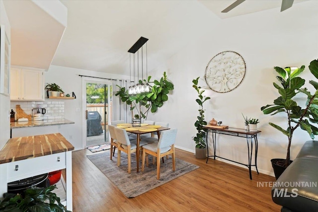 dining room featuring baseboards, lofted ceiling, light wood-style floors, and ceiling fan with notable chandelier