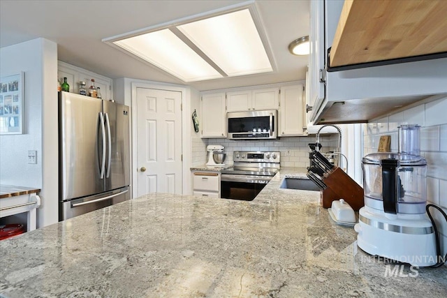 kitchen with light stone counters, a sink, decorative backsplash, white cabinets, and appliances with stainless steel finishes