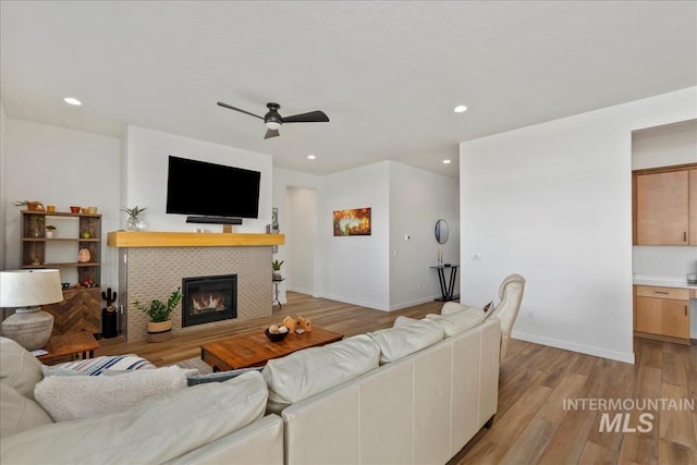 living room featuring a tiled fireplace, recessed lighting, light wood finished floors, baseboards, and ceiling fan