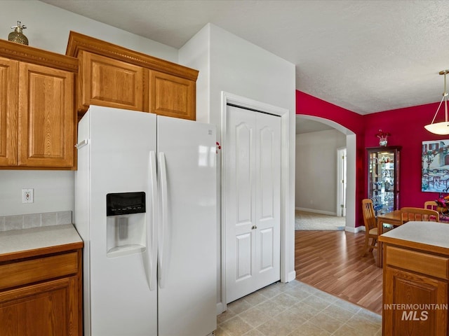 3369 W Monessen Ln, Meridian, ID 83646 - kitchen featuring white fridge with ice dispenser, arched walkways, brown cabinetry, light countertops, and pendant lighting