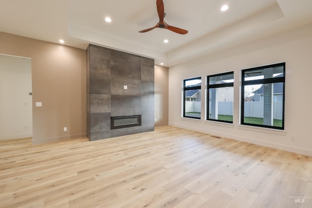 unfurnished living room with light wood-type flooring, a tray ceiling, ceiling fan, and a tiled fireplace