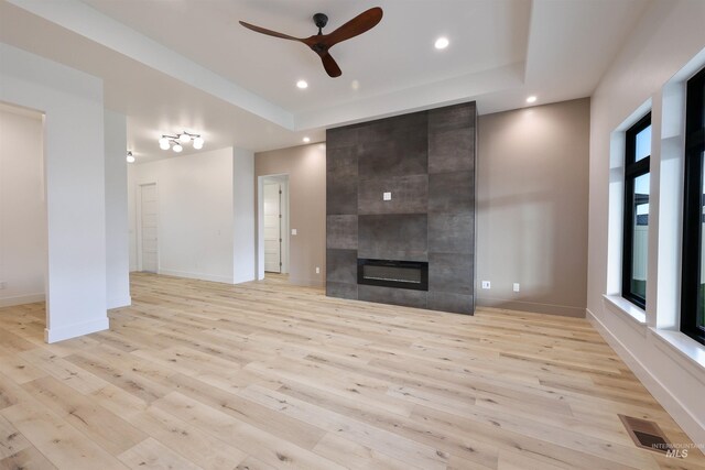 unfurnished living room featuring a fireplace, light hardwood / wood-style floors, ceiling fan, and a tray ceiling