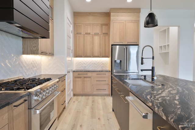 kitchen featuring hanging light fixtures, ventilation hood, dark stone countertops, appliances with stainless steel finishes, and light wood-type flooring