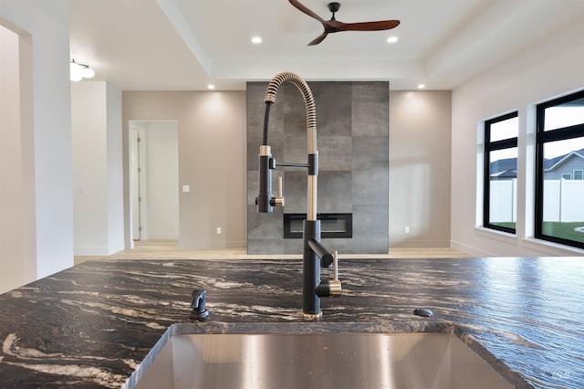 interior details with a raised ceiling, dark stone countertops, ceiling fan, and sink