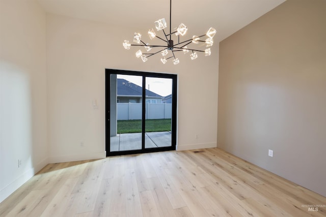 unfurnished room with a notable chandelier, light wood-type flooring, and vaulted ceiling