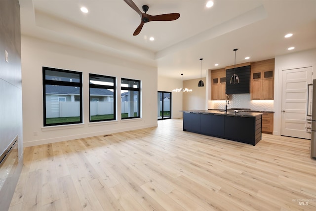 kitchen featuring backsplash, ceiling fan with notable chandelier, pendant lighting, light hardwood / wood-style floors, and an island with sink