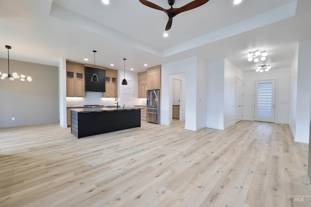 kitchen featuring stainless steel fridge, light hardwood / wood-style floors, a kitchen island with sink, and hanging light fixtures