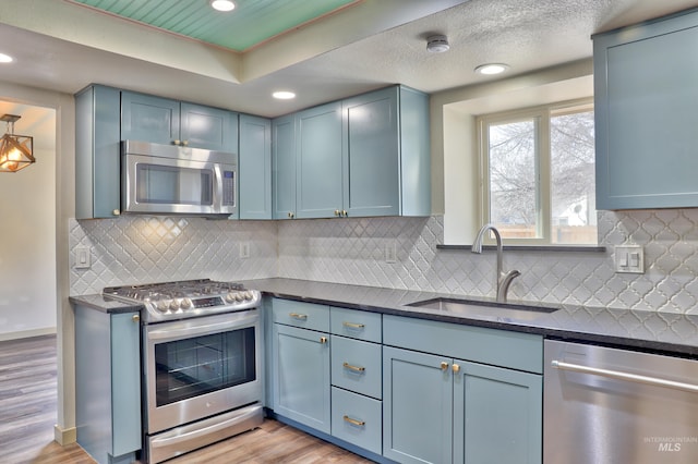 kitchen with light wood-type flooring, a sink, blue cabinetry, appliances with stainless steel finishes, and decorative backsplash