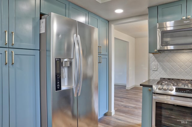 kitchen with dark countertops, blue cabinetry, light wood-type flooring, decorative backsplash, and appliances with stainless steel finishes