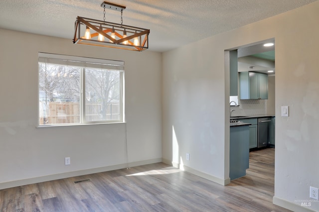 unfurnished dining area featuring visible vents, baseboards, wood finished floors, a textured ceiling, and a sink