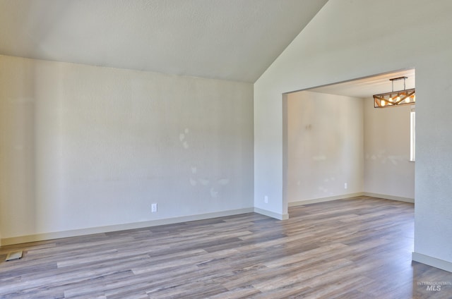 unfurnished room with baseboards, a notable chandelier, wood finished floors, and vaulted ceiling