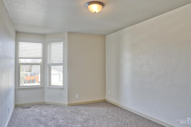 carpeted spare room featuring visible vents, a textured ceiling, and baseboards