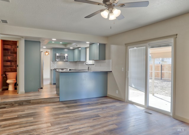 kitchen featuring visible vents, ceiling fan, appliances with stainless steel finishes, a peninsula, and light wood-style floors