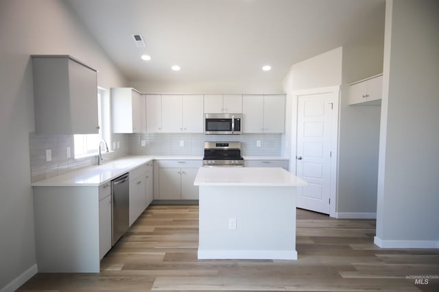 kitchen featuring stainless steel appliances, white cabinetry, a kitchen island, and lofted ceiling