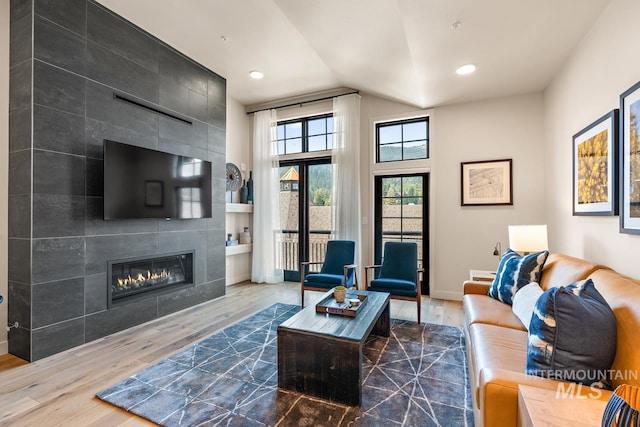 living room featuring wood-type flooring, a tile fireplace, and vaulted ceiling