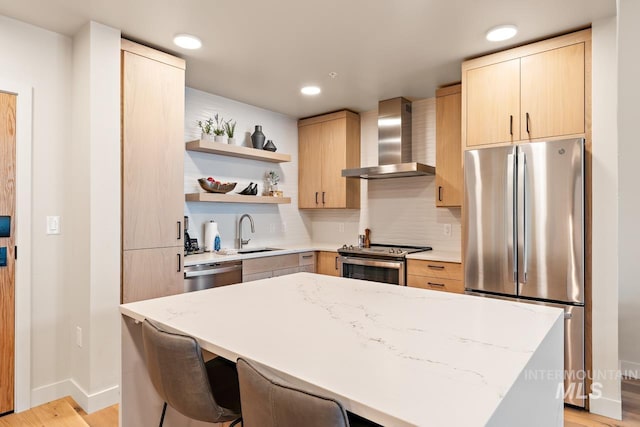 kitchen featuring light stone counters, sink, stainless steel appliances, and wall chimney exhaust hood