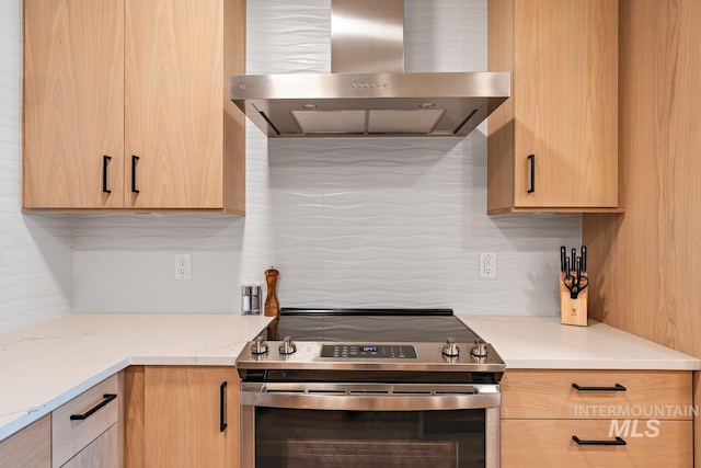 kitchen featuring light stone counters, light brown cabinets, stainless steel range with electric cooktop, and wall chimney range hood