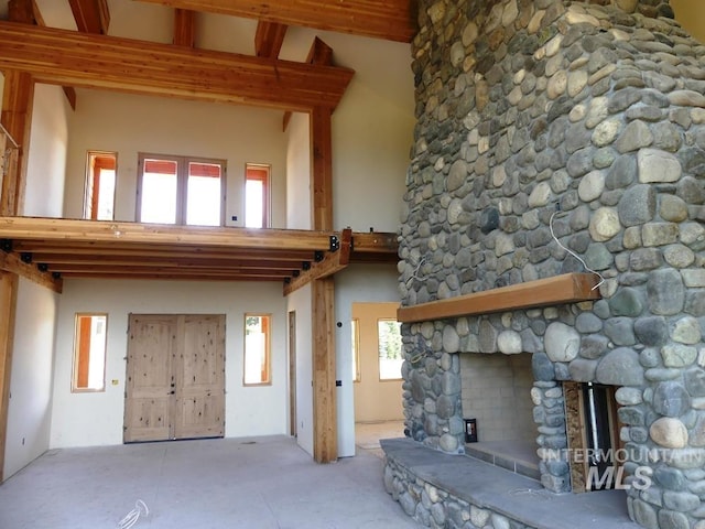 unfurnished living room with beam ceiling, a stone fireplace, and a healthy amount of sunlight