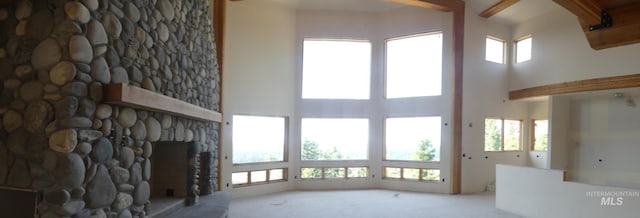 unfurnished living room featuring a stone fireplace, beam ceiling, light carpet, and a towering ceiling