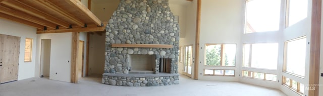 unfurnished living room featuring beam ceiling, a towering ceiling, and a fireplace