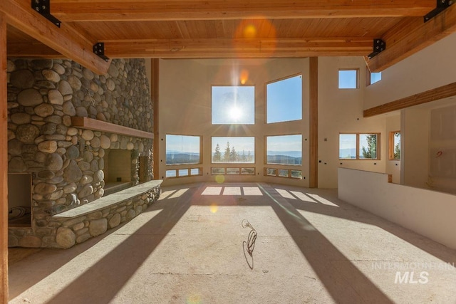 unfurnished living room featuring a towering ceiling, a stone fireplace, beamed ceiling, and wooden ceiling