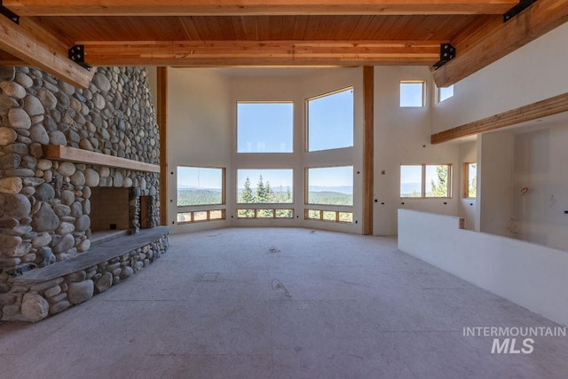 unfurnished living room with a towering ceiling, beamed ceiling, a stone fireplace, and a healthy amount of sunlight