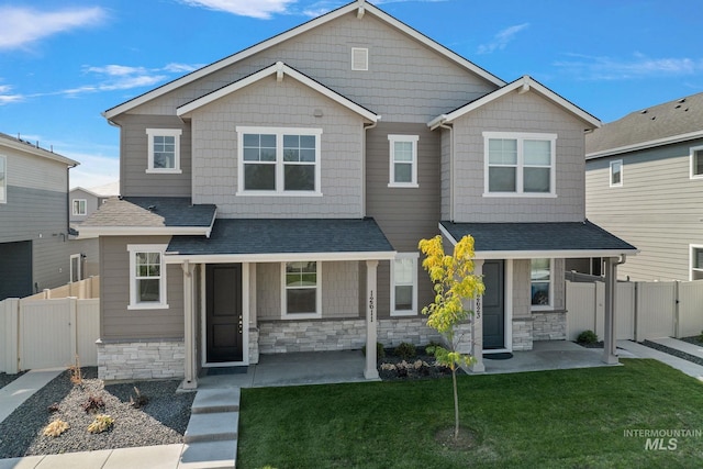 view of front of property with a shingled roof, stone siding, a gate, fence, and a front lawn