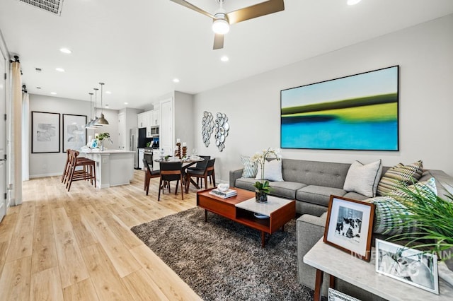 living room featuring light wood-type flooring, visible vents, ceiling fan, and recessed lighting