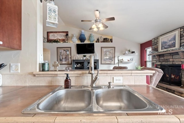 kitchen featuring a stone fireplace, sink, and vaulted ceiling