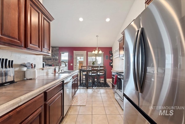 kitchen with tile counters, sink, stainless steel appliances, an inviting chandelier, and light tile patterned floors