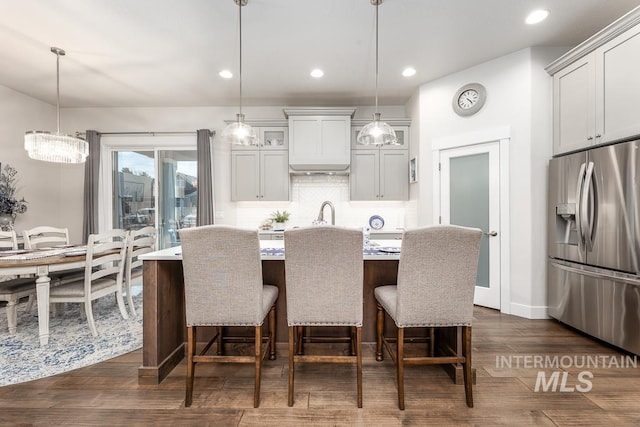 kitchen with a kitchen island with sink, a kitchen bar, backsplash, stainless steel refrigerator with ice dispenser, and light countertops