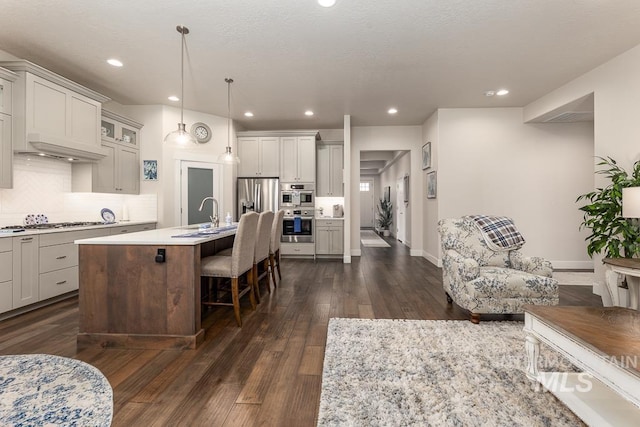 kitchen featuring an island with sink, stainless steel appliances, light countertops, dark wood-type flooring, and a breakfast bar area
