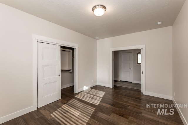 unfurnished bedroom featuring dark wood finished floors, baseboards, a textured ceiling, and a closet