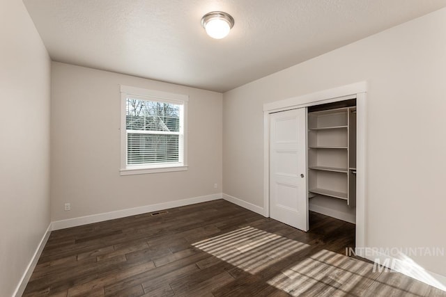 unfurnished bedroom with baseboards, dark wood-style flooring, visible vents, and a closet