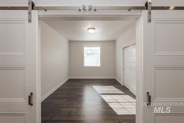 spare room with dark wood finished floors, a barn door, and baseboards