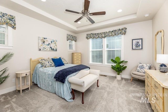 bedroom with a raised ceiling, visible vents, light colored carpet, and multiple windows