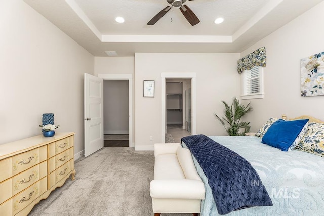 bedroom with a tray ceiling, a spacious closet, light colored carpet, and recessed lighting
