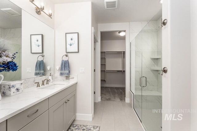 bathroom with a textured ceiling, baseboards, visible vents, a shower stall, and vanity