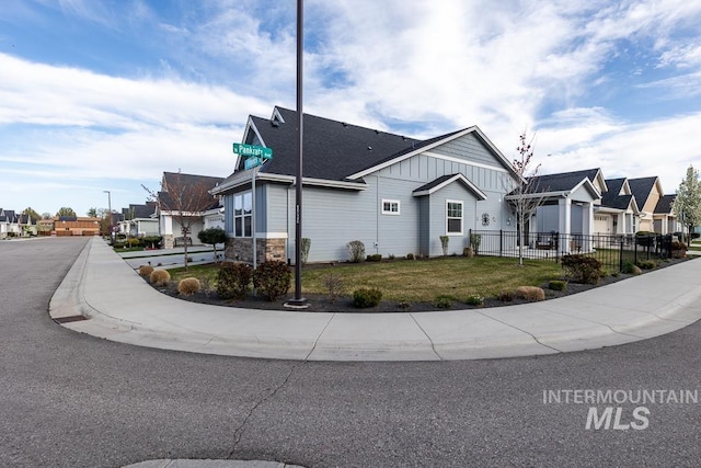 view of front of home featuring a residential view, a front lawn, stone siding, fence, and a shingled roof