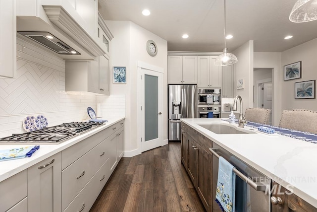 kitchen featuring a sink, stainless steel appliances, custom range hood, decorative light fixtures, and dark wood-style floors