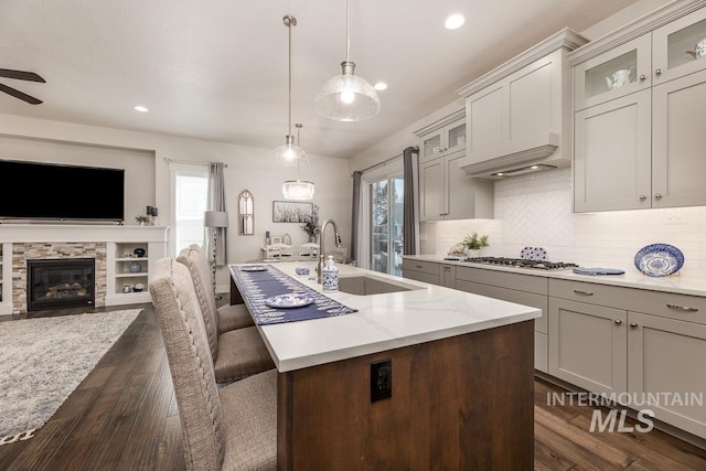 kitchen with a sink, decorative backsplash, open floor plan, a center island with sink, and dark wood-style floors