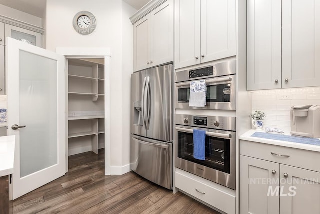 kitchen with dark wood finished floors, light countertops, backsplash, baseboards, and appliances with stainless steel finishes