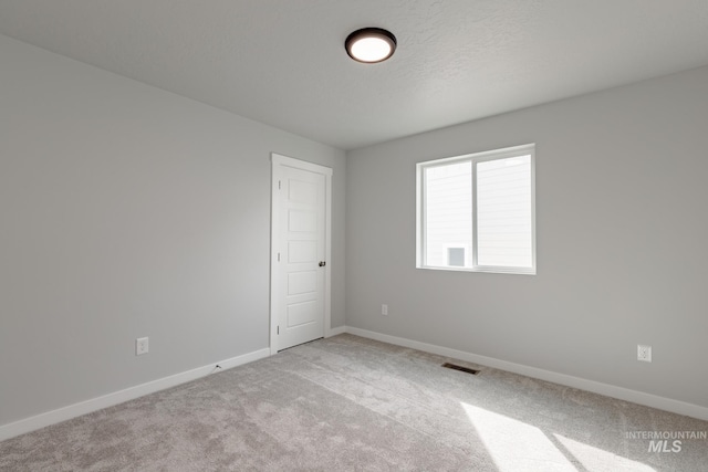 unfurnished room featuring baseboards, visible vents, a textured ceiling, and light colored carpet